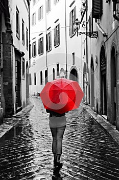 Woman with red umbrella on retro street in the old town. Wind and rain