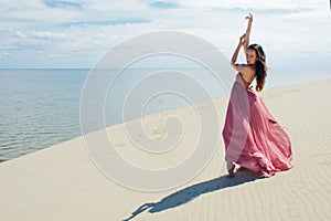 Woman in red waving dress with flying fabric runs on background of dunes. Gymnast on the back of the dune