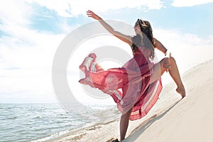 Woman in red waving dress with flying fabric runs on background of dunes.