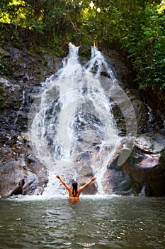 Woman refreshing herself in beautiful waterfall