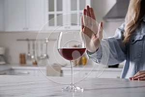 Woman refusing to drink red wine at home, closeup. Alcohol addiction treatment