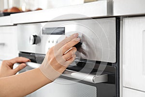Woman regulating cooking mode on oven panel in kitchen
