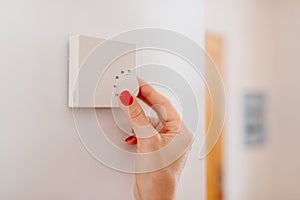 Woman regulating temperature on home heating thermostat