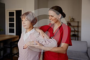 Woman rehabilitation therapist assisting senior female exercising at home