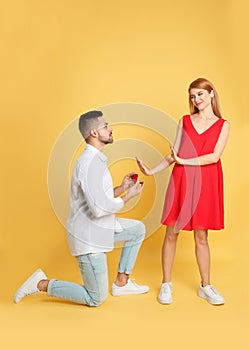 Woman rejecting engagement ring from boyfriend on yellow background