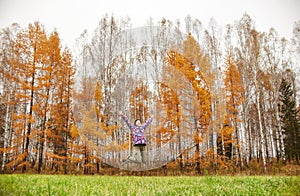 Woman rejoices at the arrival of autumn. Girl in a field near the yellow autumn forest, autumn came, the emotion of joy