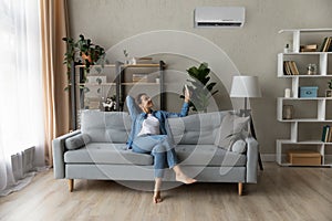 Woman relax on couch holding remote controller turns on airconditioner