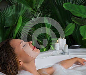 A woman relaxes in hot bath tub with soap foam