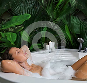 A woman relaxes in hot bath tub with soap foam