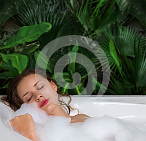 A woman relaxes in hot bath tub with soap foam