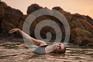 Woman relaxes in sea at sunset, serene natural swim, embodies wellness, eco therapy. Fitness, solitude with aquatic