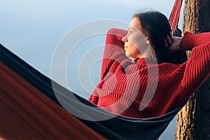 Woman relaxing admiring lake lying in hammock in forest at sunset on nature.