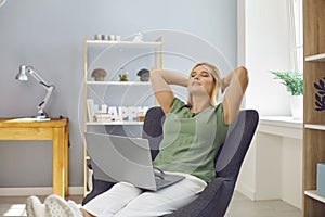 Woman relaxing in an armchair with computer on lap, feeling satisfied after finishing work