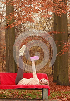 Woman relaxing in autumn fall park reading book.