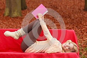 Woman relaxing in autumn fall park reading book.