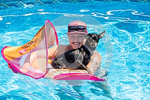 Woman relaxing with black pinscher dog on a flotation device in the swimming pool