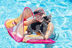 Woman relaxing with black pinscher dog on a flotation device in the swimming pool