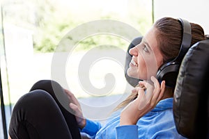 Woman Relaxing In Chair At Home Listening To Music Or Podcast Music On Wireless Earphones