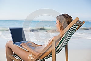 Woman relaxing in deck chair on the beach using laptop