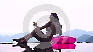 Woman relaxing at the edge of infinity swimming pool at resort rubber ring hills and mountain view