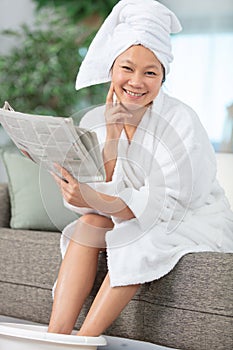 woman relaxing with feet in foot bath reading newspaper