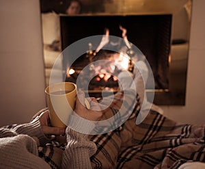 Woman relaxing by the fireplace warming up feet in woolen with a cup of hot drink socks and blanket