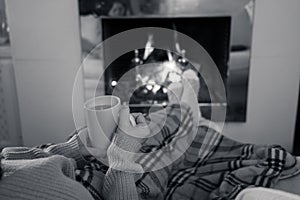 Woman relaxing by the fireplace warming up feet in woolen with a cup of hot drink socks and blanket