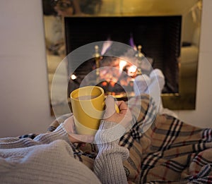 Woman relaxing by the fireplace warming up feet in woolen with a cup of hot drink socks and blanket