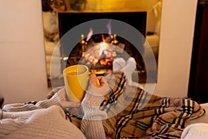 Woman relaxing by the fireplace warming up feet in woolen with a cup of hot drink socks and blanket