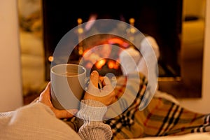 Woman relaxing by the fireplace warming up feet in woolen with a cup of hot drink socks and blanket