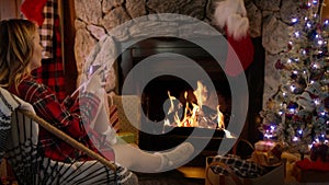 Woman relaxing by glowing burning fire and warming up by hot tea or chocolate 4K