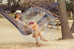 Woman relaxing in a hammock on the beach reading a book