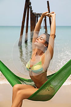 Woman is relaxing in the hammock hanging on old beams from the broken pier