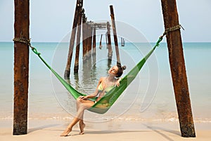 Woman is relaxing in the hammock hanging on old beams from the broken pier