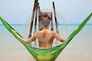 Woman is relaxing in the hammock hanging on old beams from the broken pier