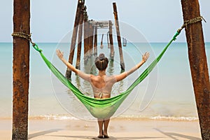 Woman is relaxing in the hammock hanging on old beams from the broken pier