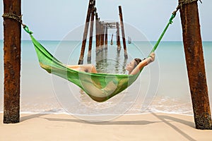 Woman is relaxing in the hammock hanging on old beams from the broken pier