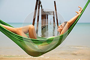 Woman is relaxing in the hammock hanging on old beams from the broken pier