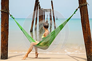 Woman is relaxing in the hammock hanging on old beams from the broken pier