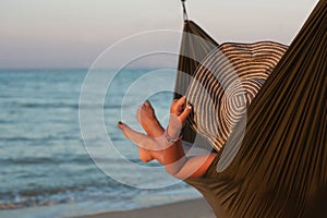 Woman relaxing on hammock with hat sunbathing on vacation. Against the background of the sea in the setting sun.