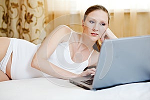 Woman relaxing with her laptop on a bed at home