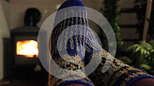 Woman relaxing at home by a fireplace, warming feet in knitted socks. Cozy place