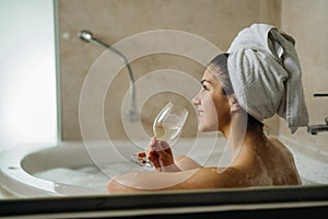Woman relaxing at home in the hot tub bath ritual,drinking wine.Relaxing spa night in bathroom.Good personal hygiene routine.Skin,