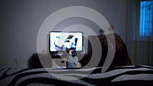 Woman relaxing at home on the sofa, switches tv channels in the evening, back view