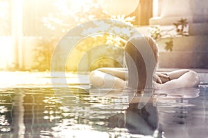 Woman relaxing in hotel spa swimming pool looking at view with sunlight and copy space