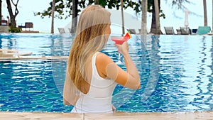 Woman relaxing in infinity pool at luxurious hotel, take glass with tropical cocktail