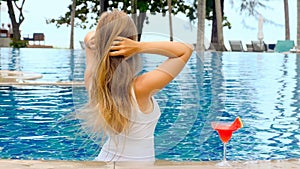 Woman relaxing in infinity pool, touching hair, enjoying nature and sea view