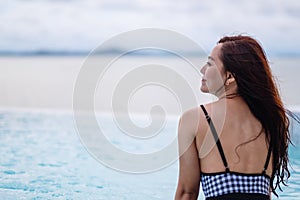 A woman relaxing in infinity swimming pool looking at a beautiful sea view