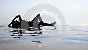 Woman relaxing in infinity swimming pool looking at view