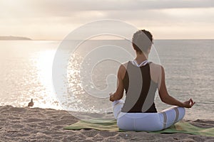 Woman relaxing in lotus pose on the beach. Meditation near the sea at sunrise